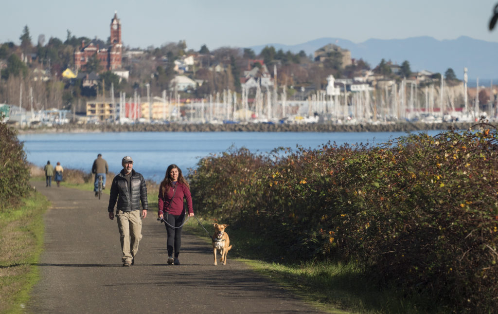 A couple and a dog walk along the Larry Scott Trail with Port Townsend in the background
