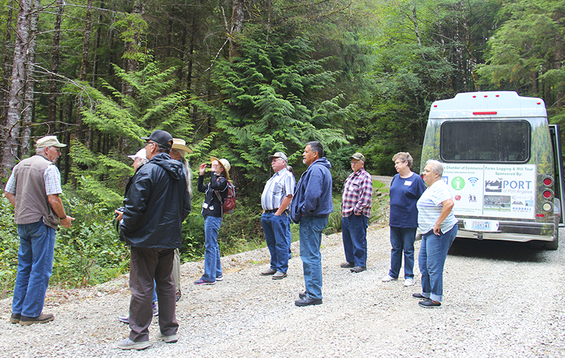 Visitors listen to a guide on the Forks Logging and Mill tour with the tour bus in the background