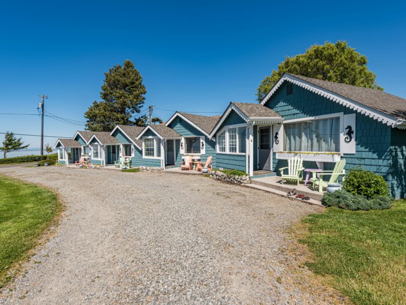 A row of blue cottages with a gravel driveway in front.