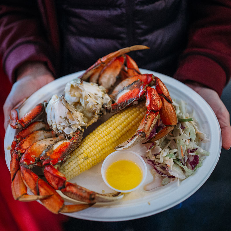 a paper plate with crab, corn, slaw, and melted butter