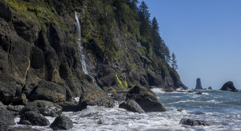 Strawberry Bay Falls plunges into the Pacific Ocean with sea stacks in the background