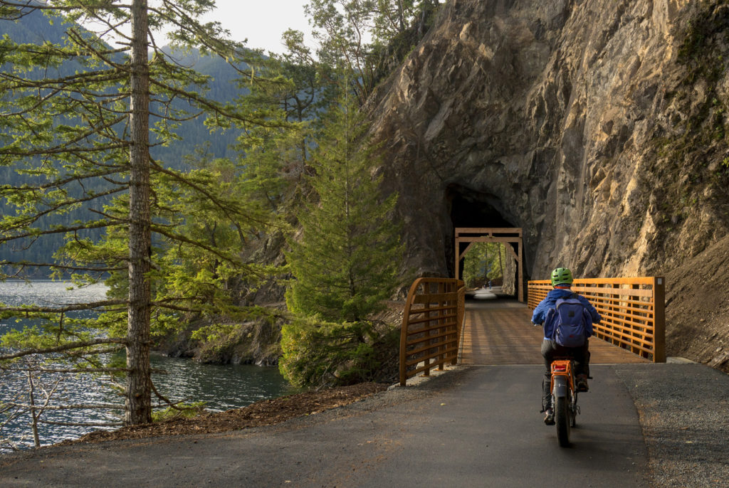 A bicyclist rides on a trail with a bridge leading to a tunnel.
