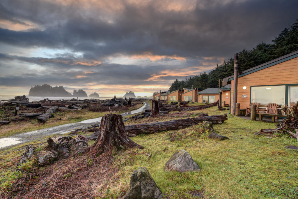 Cabins on the beach with dark clouds above and seastacks in the background
