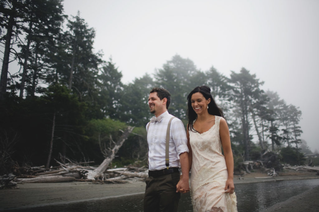 A couple walks on the beach a rainy, foggy wedding day.