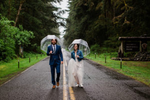A wedding couple walks with umbrellas
