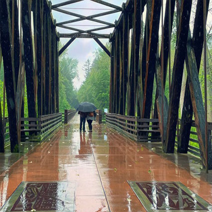 A couple walks with an umbrella on a wet footbridge in the rain
