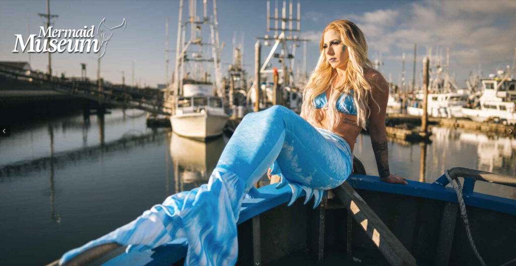 A woman dressed as a mermaid posing on a boat in a marina in the sunshine.