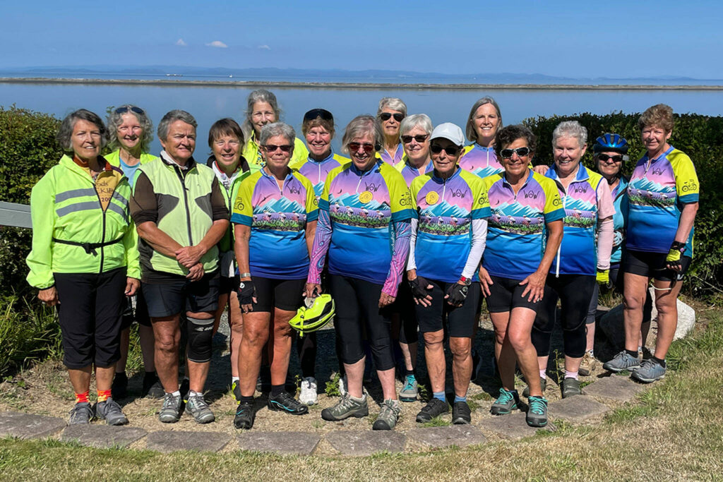 Photo of women in the Women on Wheels bike riding group in front of large body of water - Bicycling Adventures Through the Sequim-Dungeness Valley