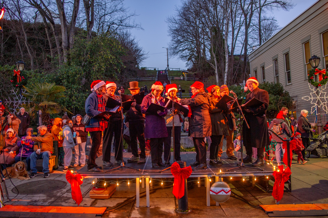 Photo of Port Townsend Carolers singing while surrounded by holiday decor and cheerful people in downtown Port Townsend, WA - Delight in Holiday Lights on the Olympic Peninsula