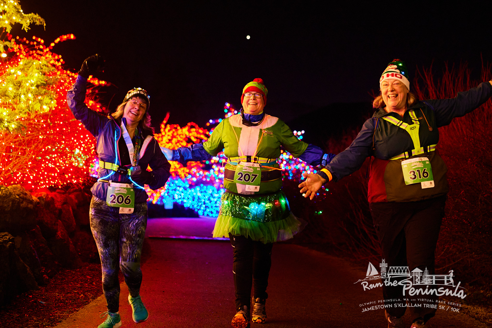 Photo of runners wearing holiday accessories with Christmas lights in the background during the Run the Peninsula Jamestown S'Klallam Tribe 5k / 10k event