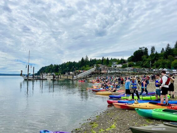 Photo of the Fjordin Crossing race before it starts as the kayaks line up on the shore of the Hood Canal in Washington state on the Olympic Peninsula